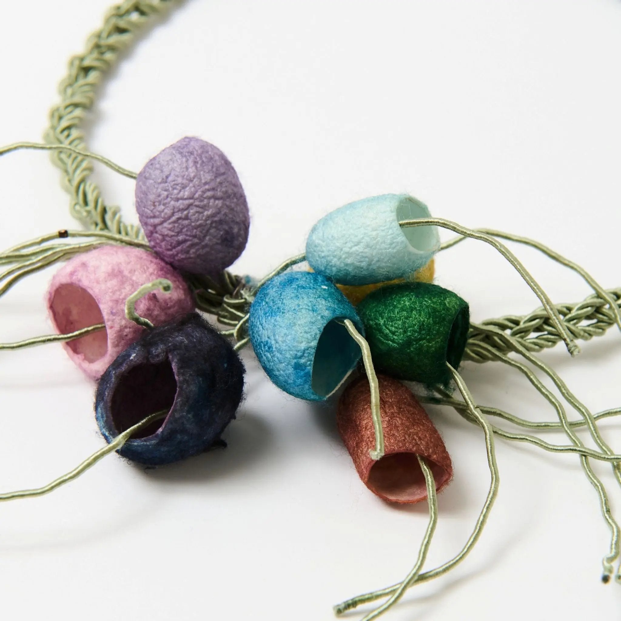 Close up of a colourful necklace with textured silk cocoons on a white background