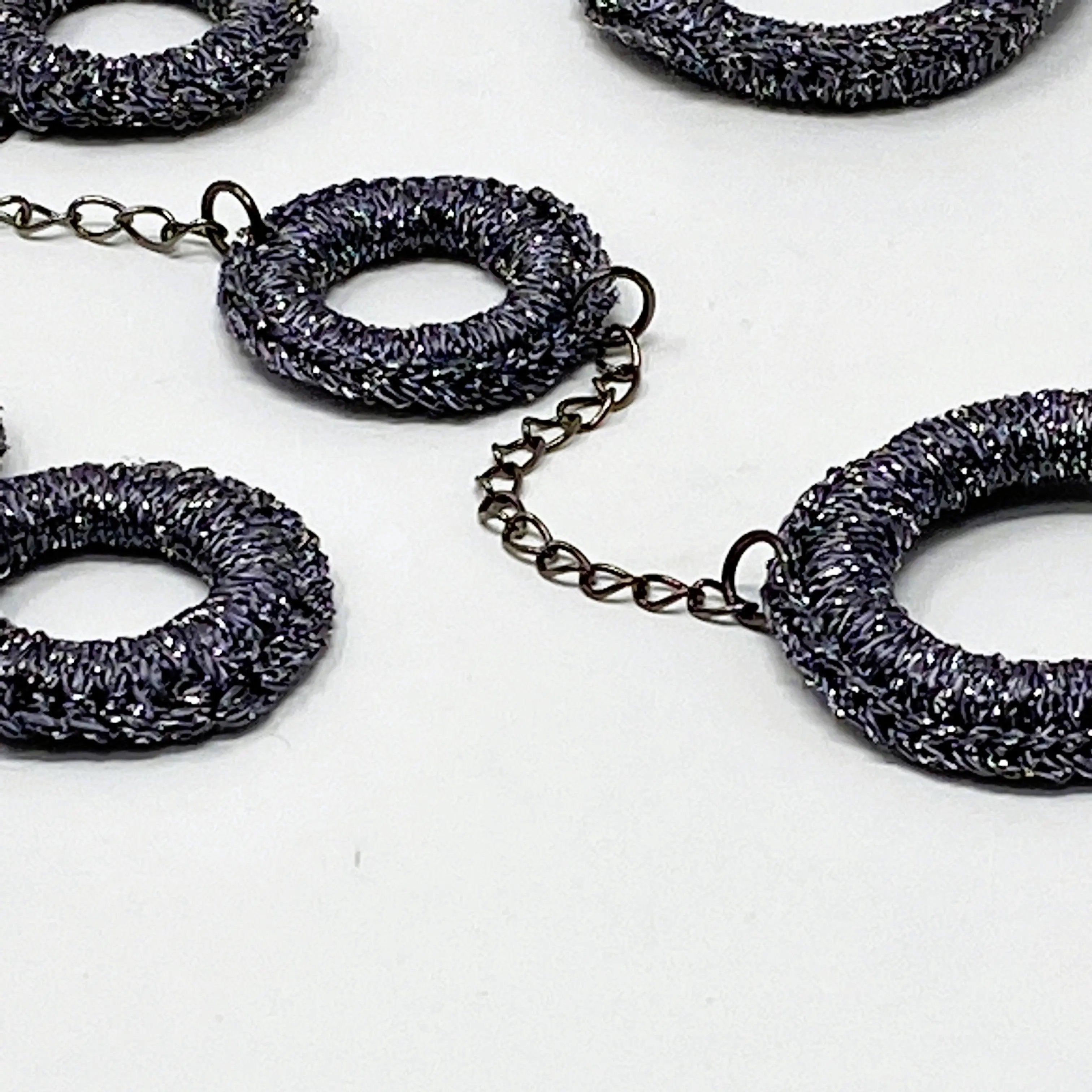Detailed close-up showing the textured finish of the charcoal circular elements and interlinking chain of the necklace.