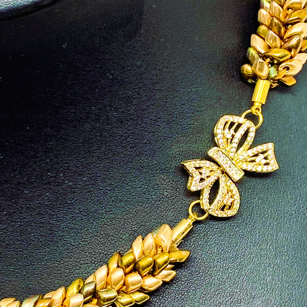 Close-up of the Maris gold bow clasp set with clear crystals, between champagne and bronze magatama beadwork - Lodorfo