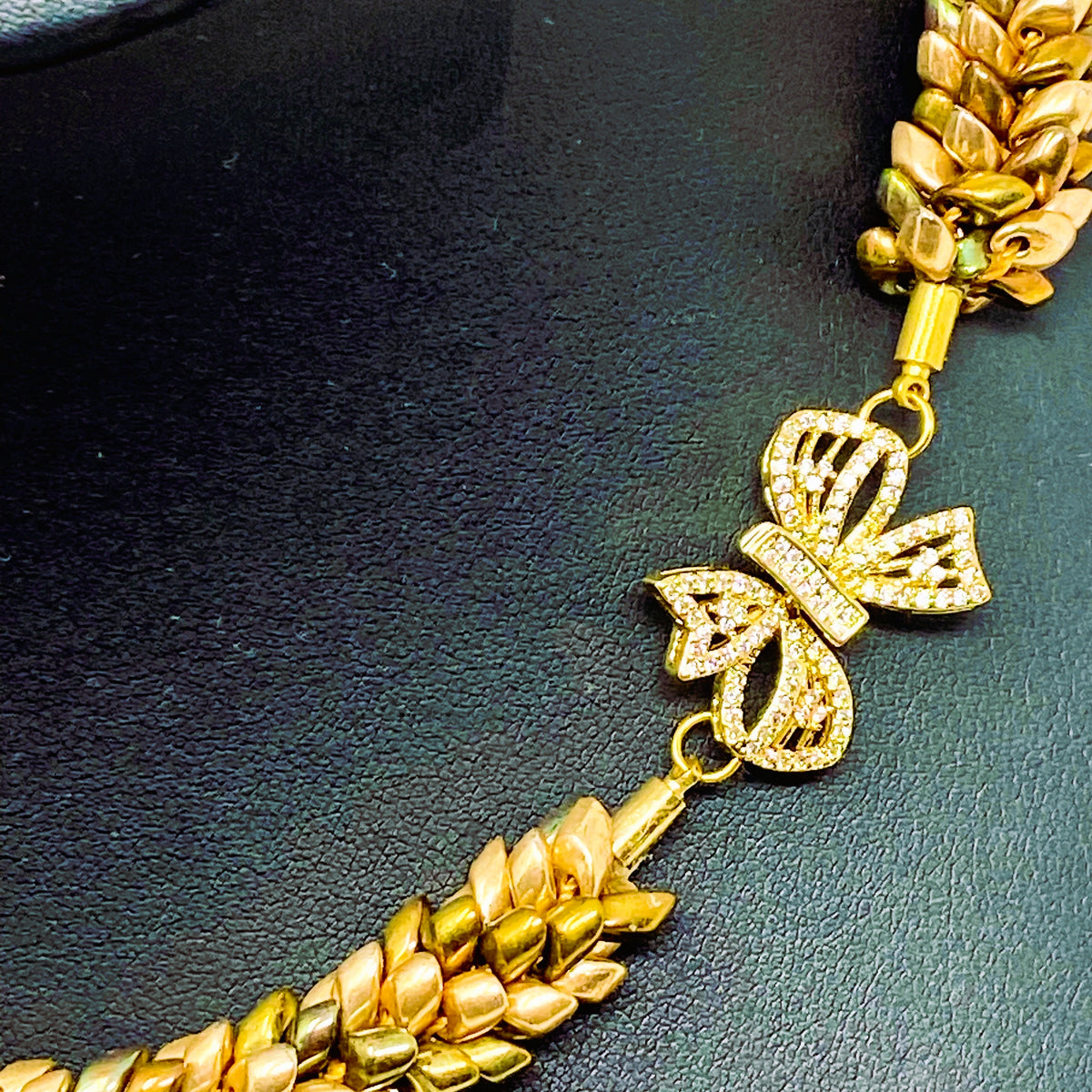 Close-up of the Maris gold bow clasp set with clear crystals, between champagne and bronze magatama beadwork - Lodorfo