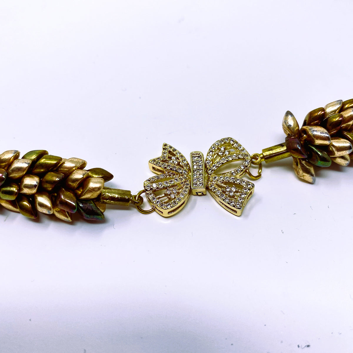 Close-up of the Maris crystal bow clasp joining two lengths of braided magatama beads in champagne, olive and bronze - Lodorfo