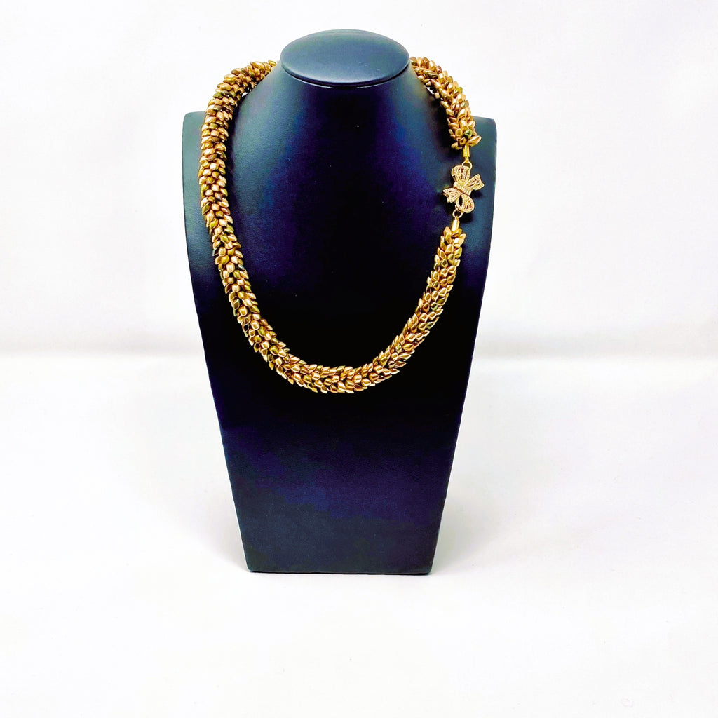 The Maris magatama beaded collar necklace in champagne, olive and bronze with a gold bow clasp, on a black display bust - Lodorfo