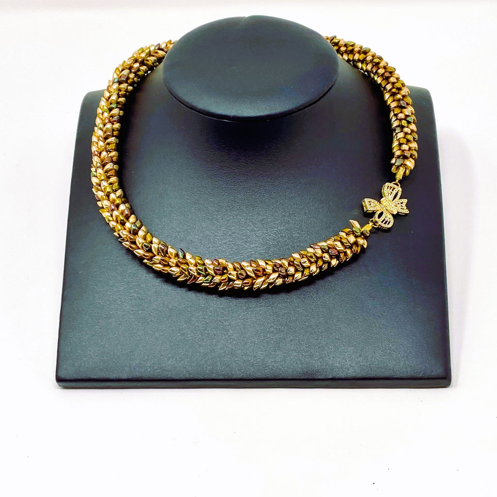 The Maris magatama beaded collar necklace in champagne, olive and bronze on a grey display stand, handmade UK - Lodorfo