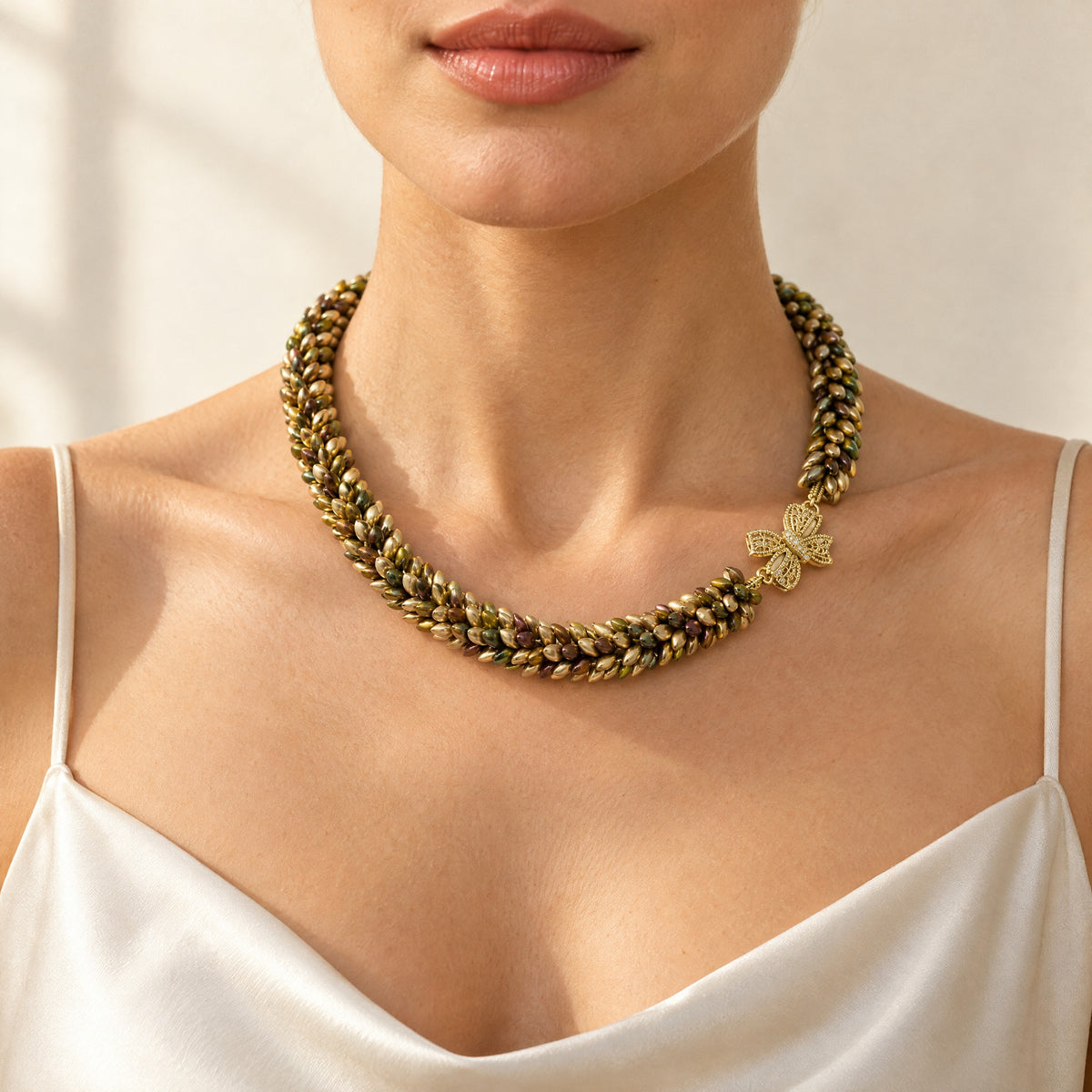 Woman wearing the Maris magatama beaded collar necklace in champagne, olive and bronze with a gold bow clasp, handmade UK - Lodorfo