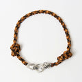 The Kaelis burnt orange and black wave-braided necklace with silver tiger head clasp, laid flat - Lodorfo