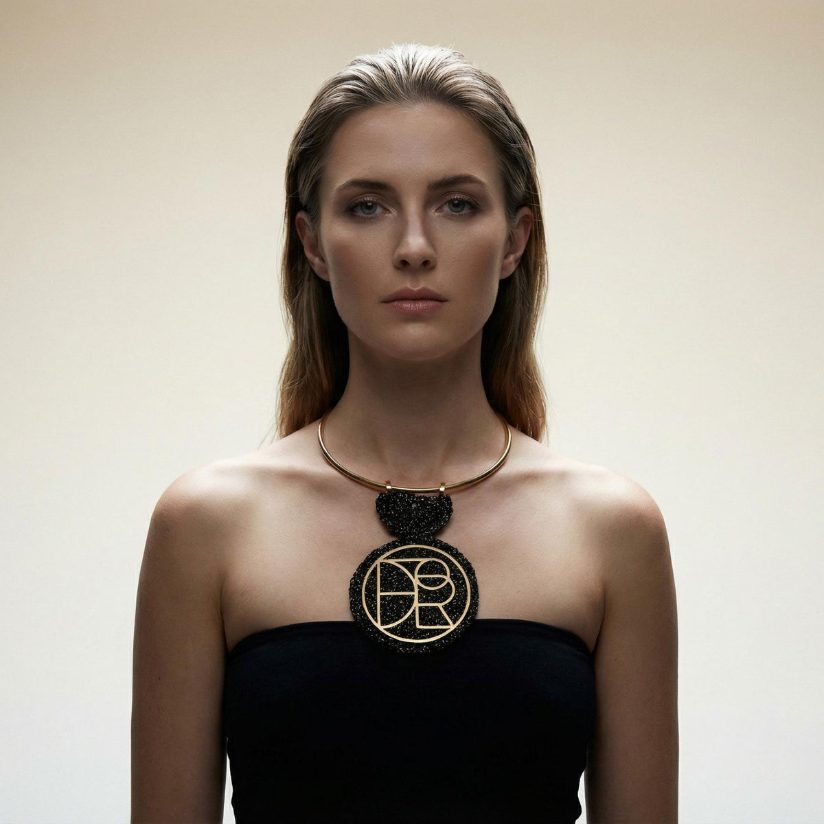 Woman in a black strapless top wearing the Orion black and gold crochet geometric pendant on a gold torque collar - Lodorfo