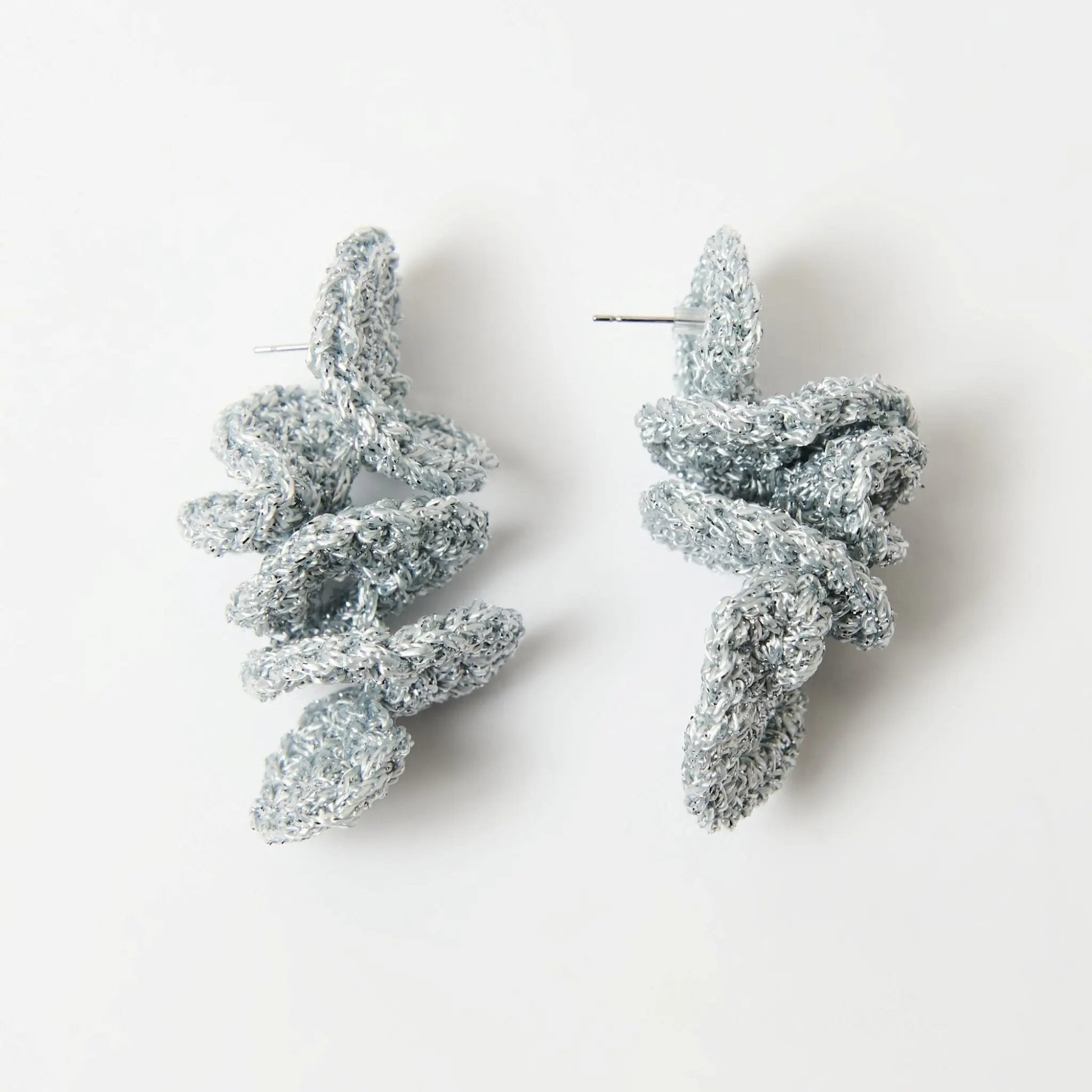 Statement spiral earrings in silver yarn with visible earring posts, highlighting their handcrafted, textural form.