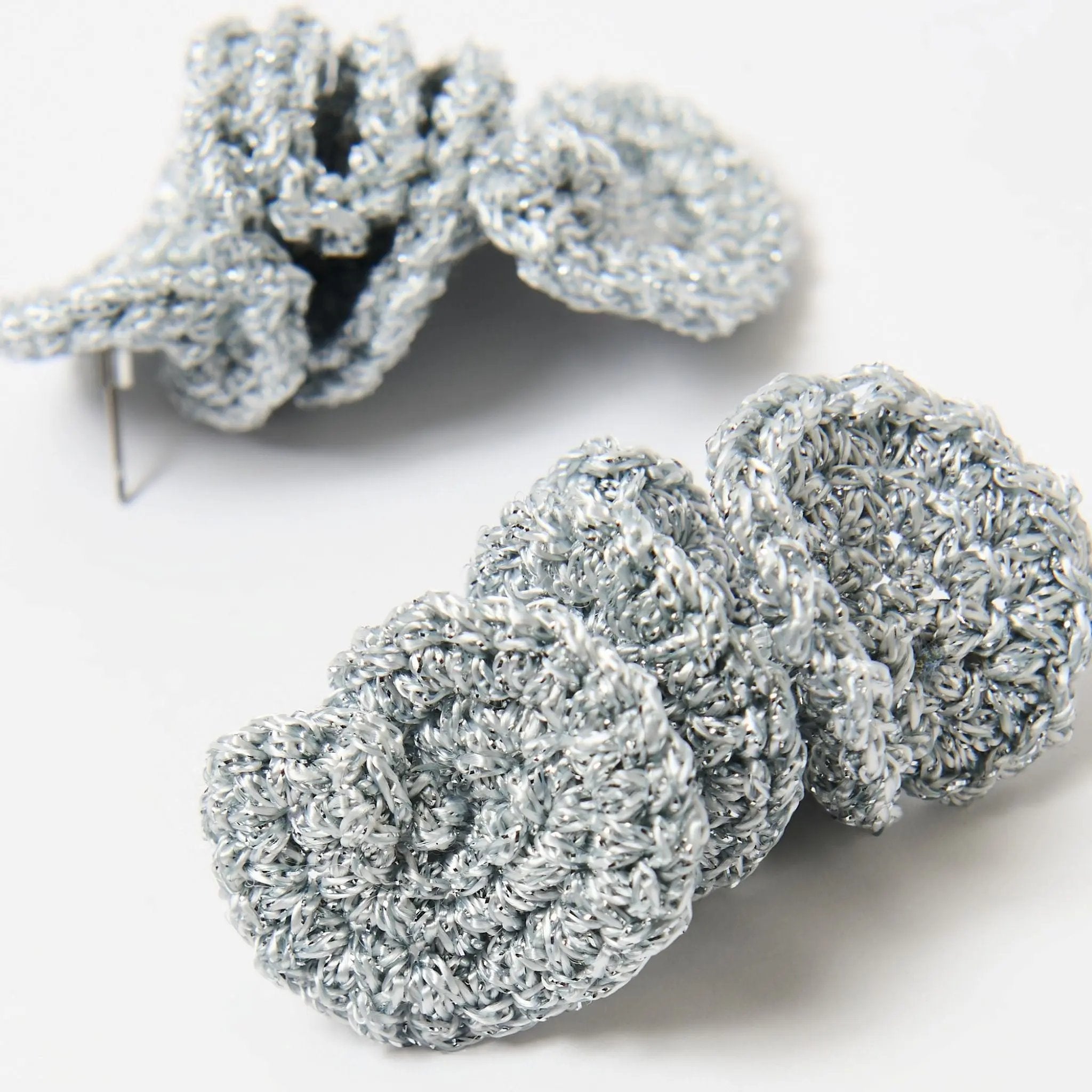 Detailed close-up of coiled silver spiral earrings, capturing the intricate loops and reflective silver metallic thread.