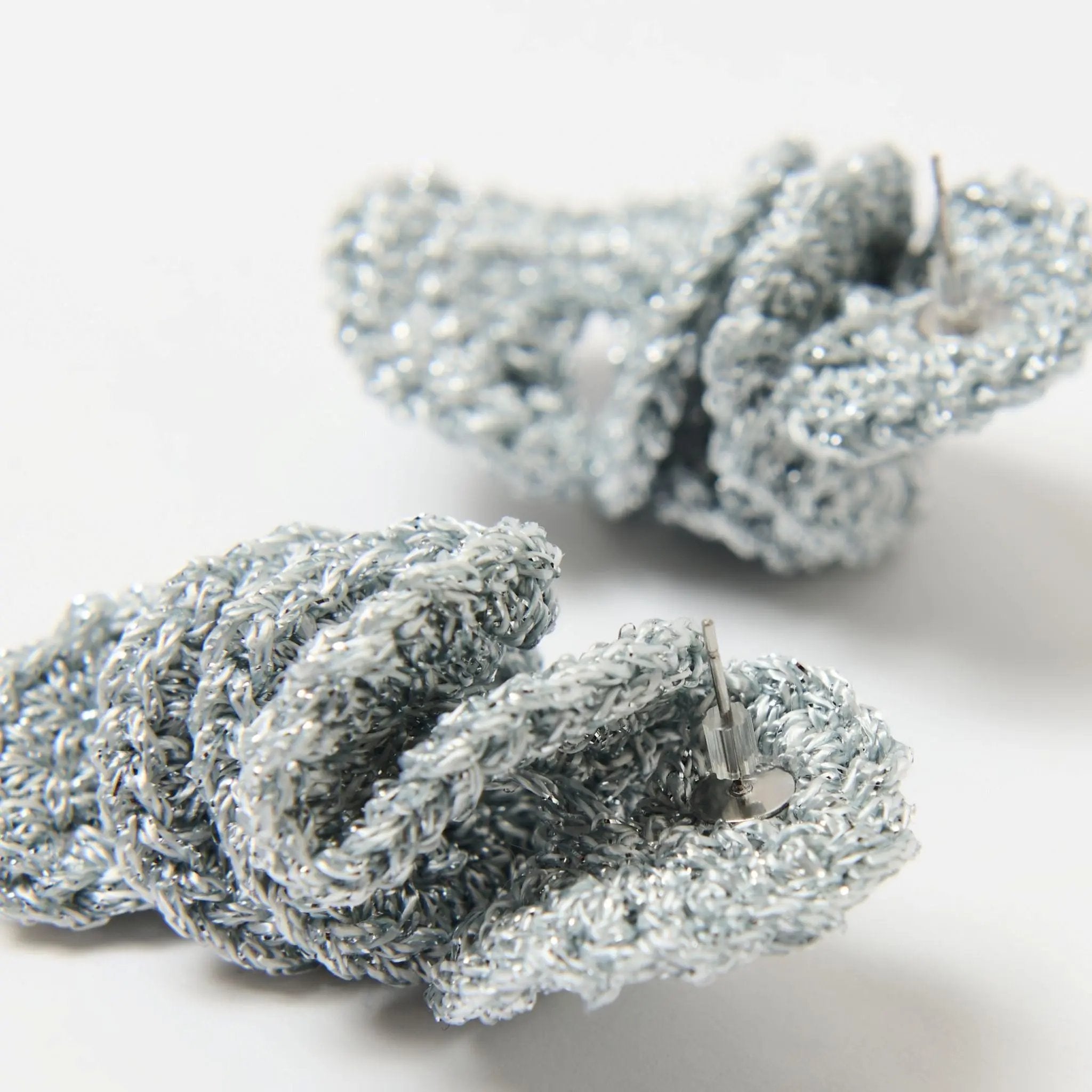 Close-up of handcrafted silver spiral earrings with stud posts, showcasing the textured, shimmering knit pattern and silver metallic sheen.