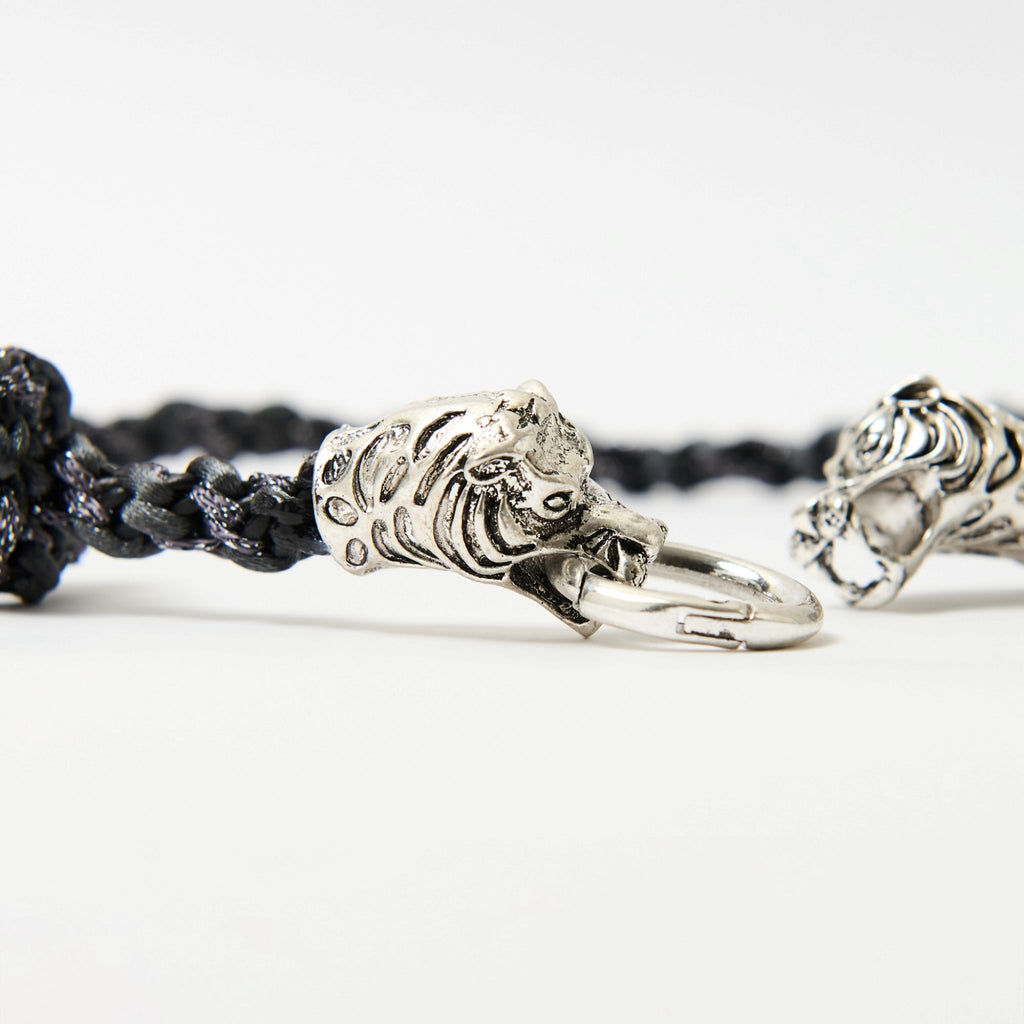 Close-up of a black braided cord necklace featuring a silver tiger head clasp with intricate detailing, each head gripping a central metal ring.