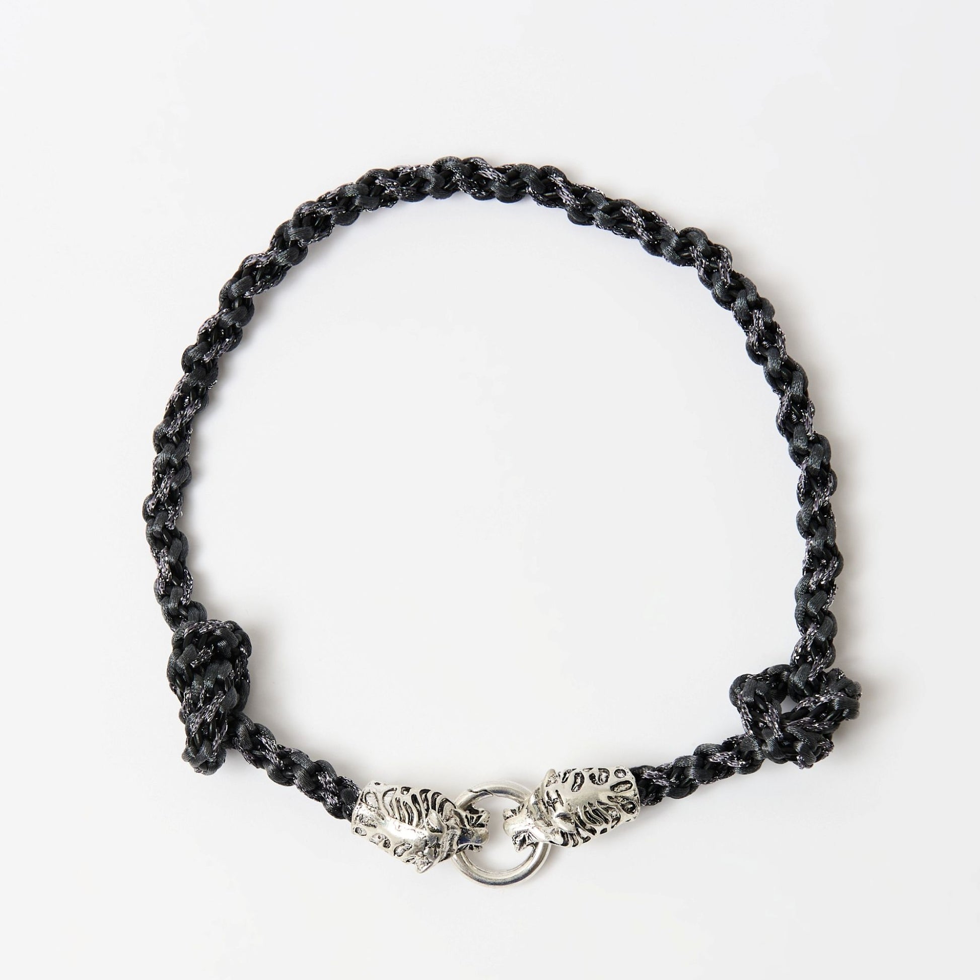 Top-down view of a black braided necklace with a silver tiger head clasp and knot detailing on each side.