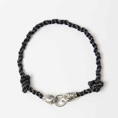 Top-down view of a black braided necklace with a silver tiger head clasp and knot detailing on each side.