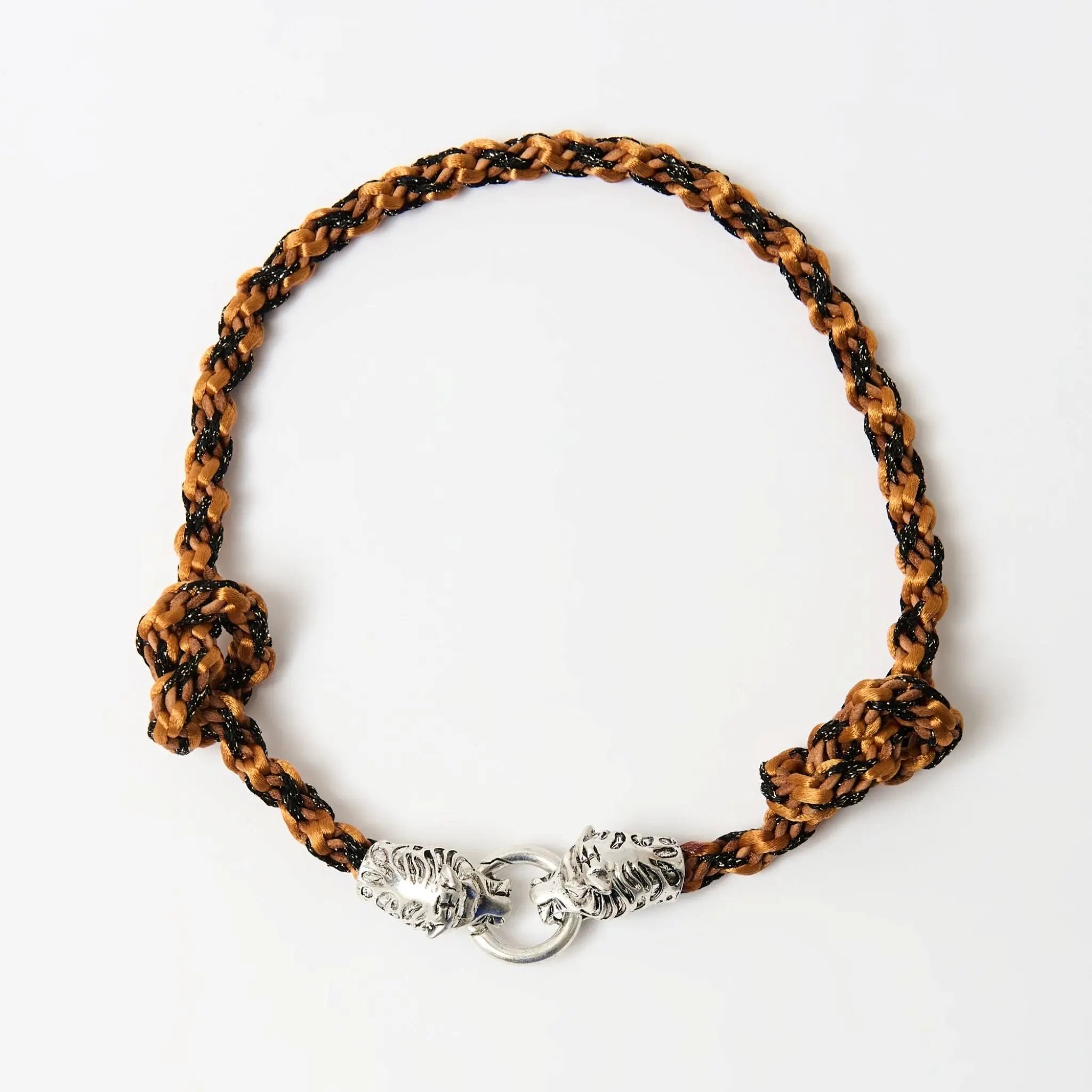 Top-down view of a braided necklace  in warn orange tones with a silver tiger head clasp and knot detailing on each side.