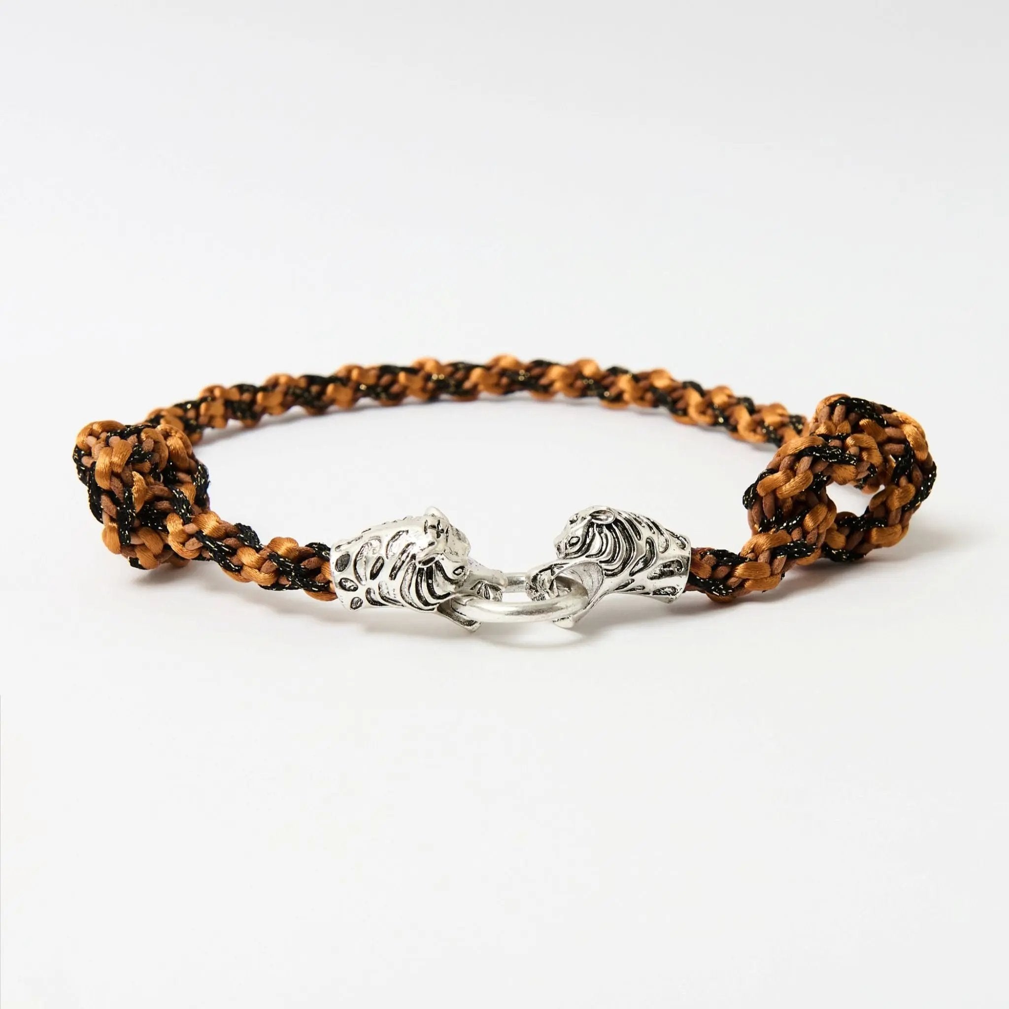 Angled view of a braided necklace in warm orange tones showing the dimensional texture of the cord and the detailed silver tiger clasp.