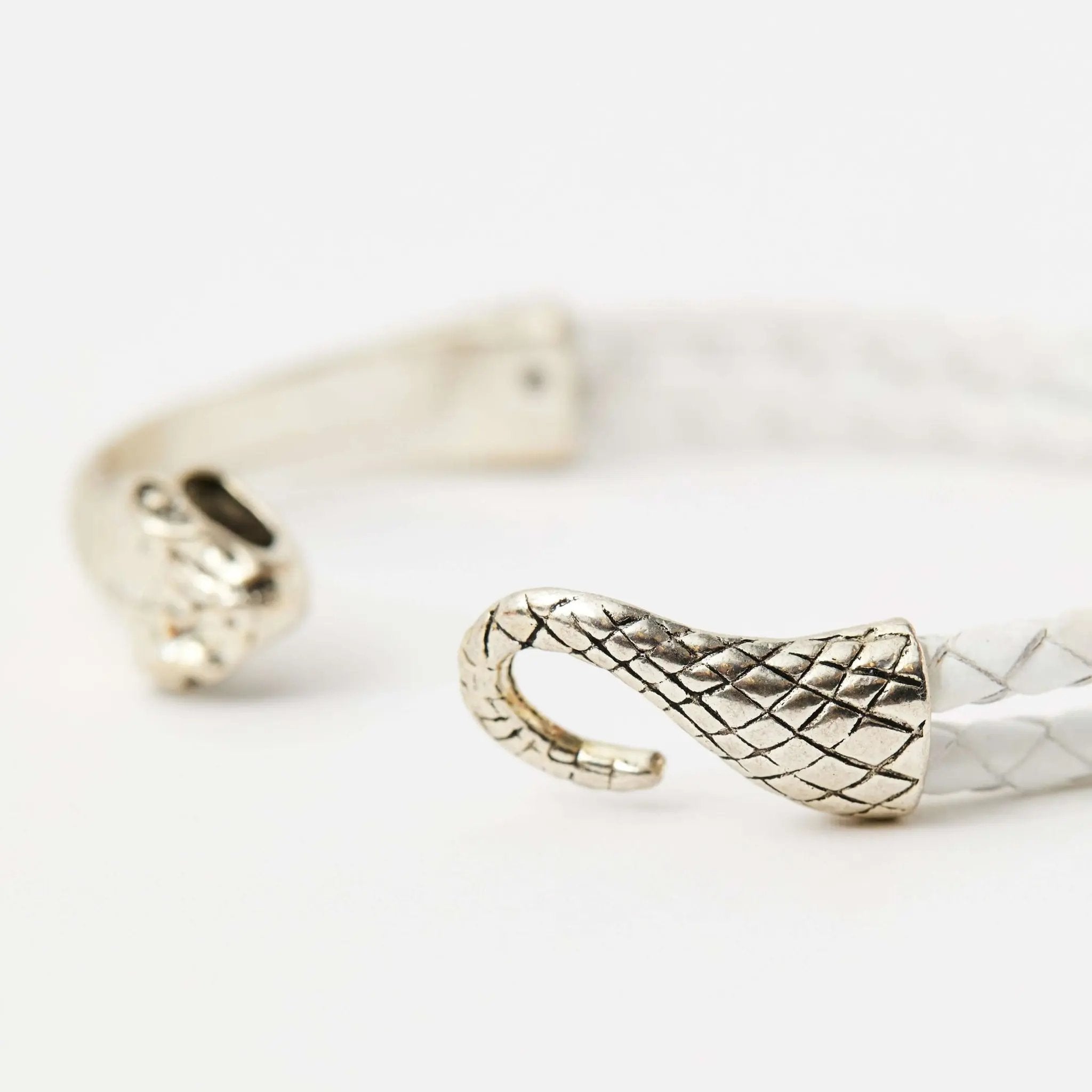 Close up of the clasp of a white braided leather bracelet with a silver snake head clasp, featuring intricate scale details and a sleek, minimalistic design.