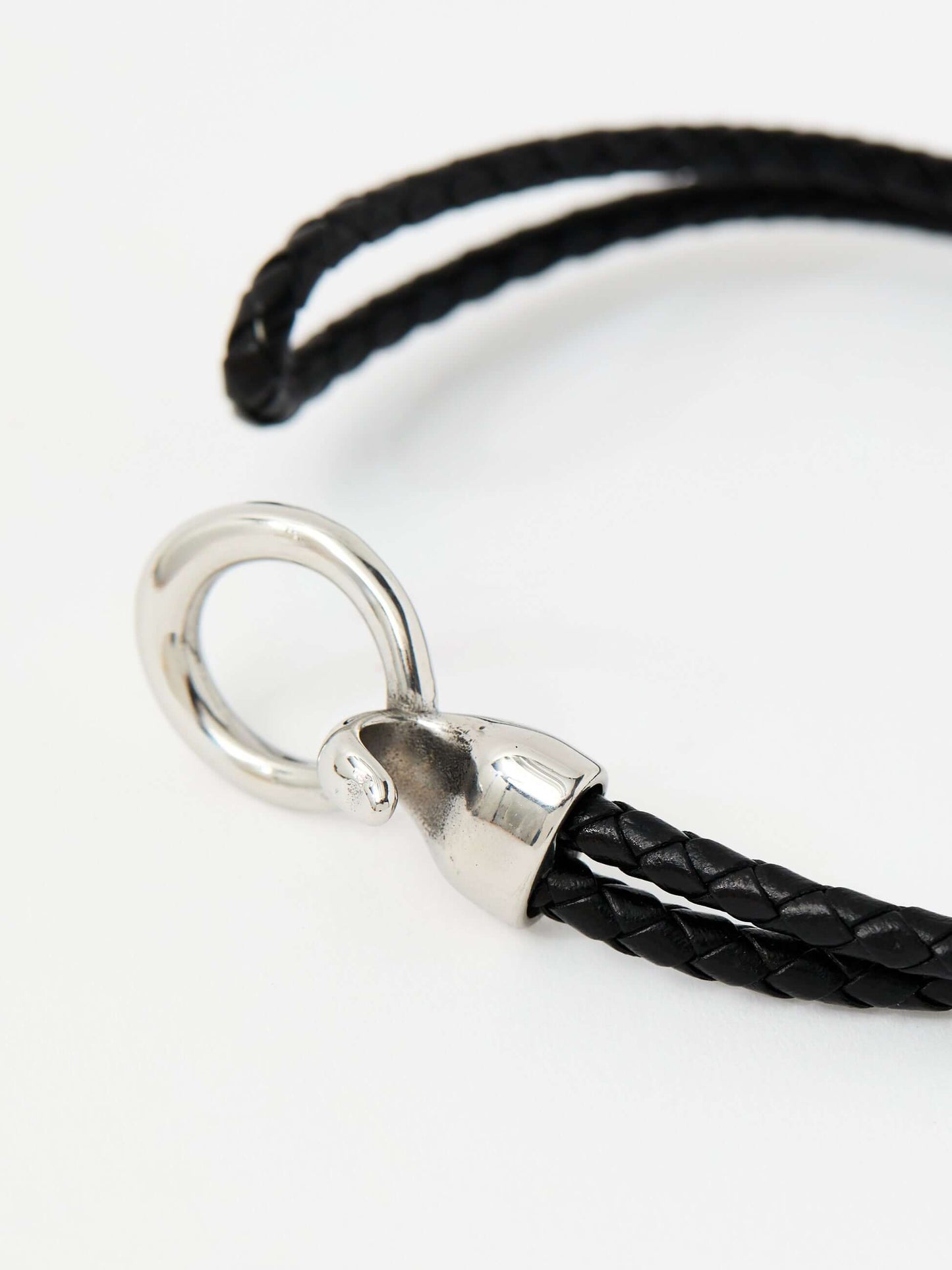 Closeup of a black braided leather bracelet with a sleek silver loop and knot clasp, showcasing a modern and minimalist style.