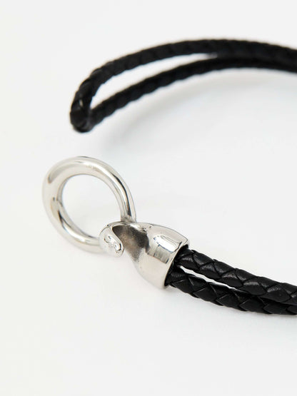 Closeup of a black braided leather bracelet with a sleek silver loop and knot clasp, showcasing a modern and minimalist style.