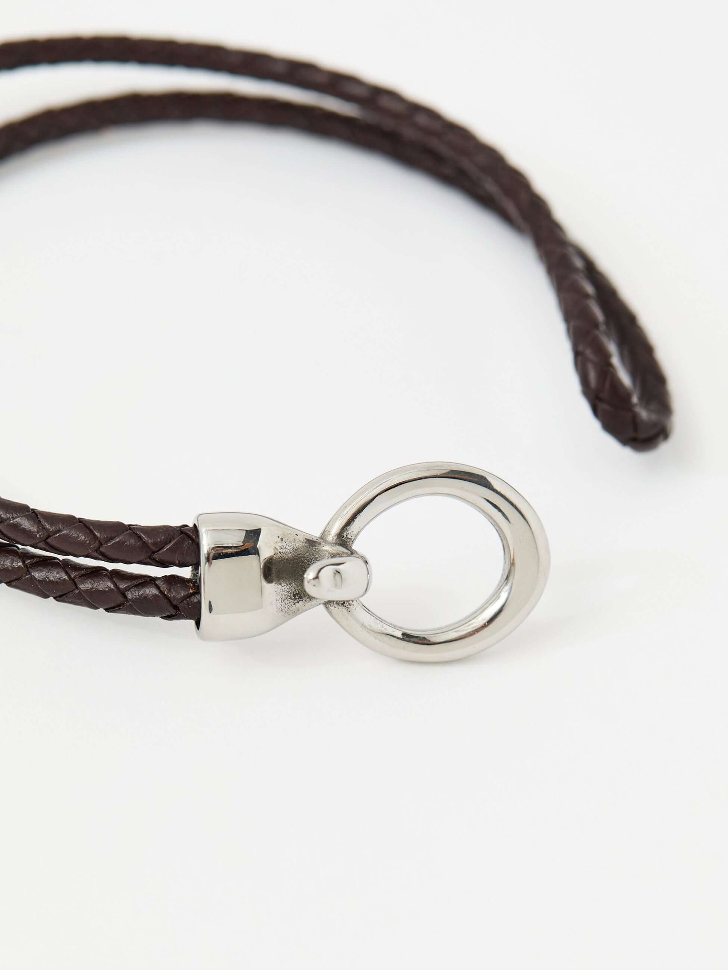 Closeup of a brown braided leather bracelet with a sleek silver loop and knot clasp, showcasing a modern and minimalist style.