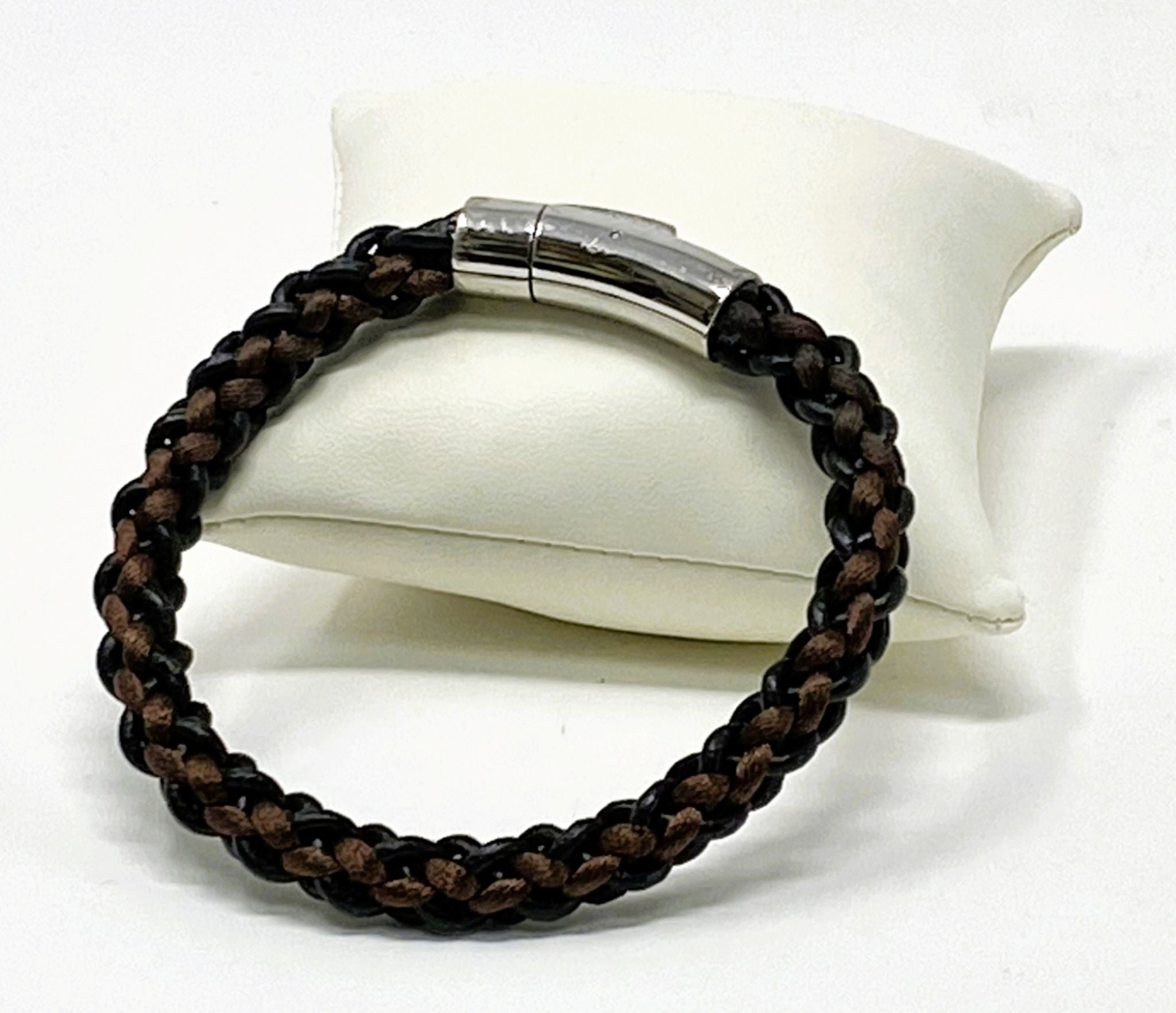 Brown braided leather bracelet with silver clasp on a white cushion