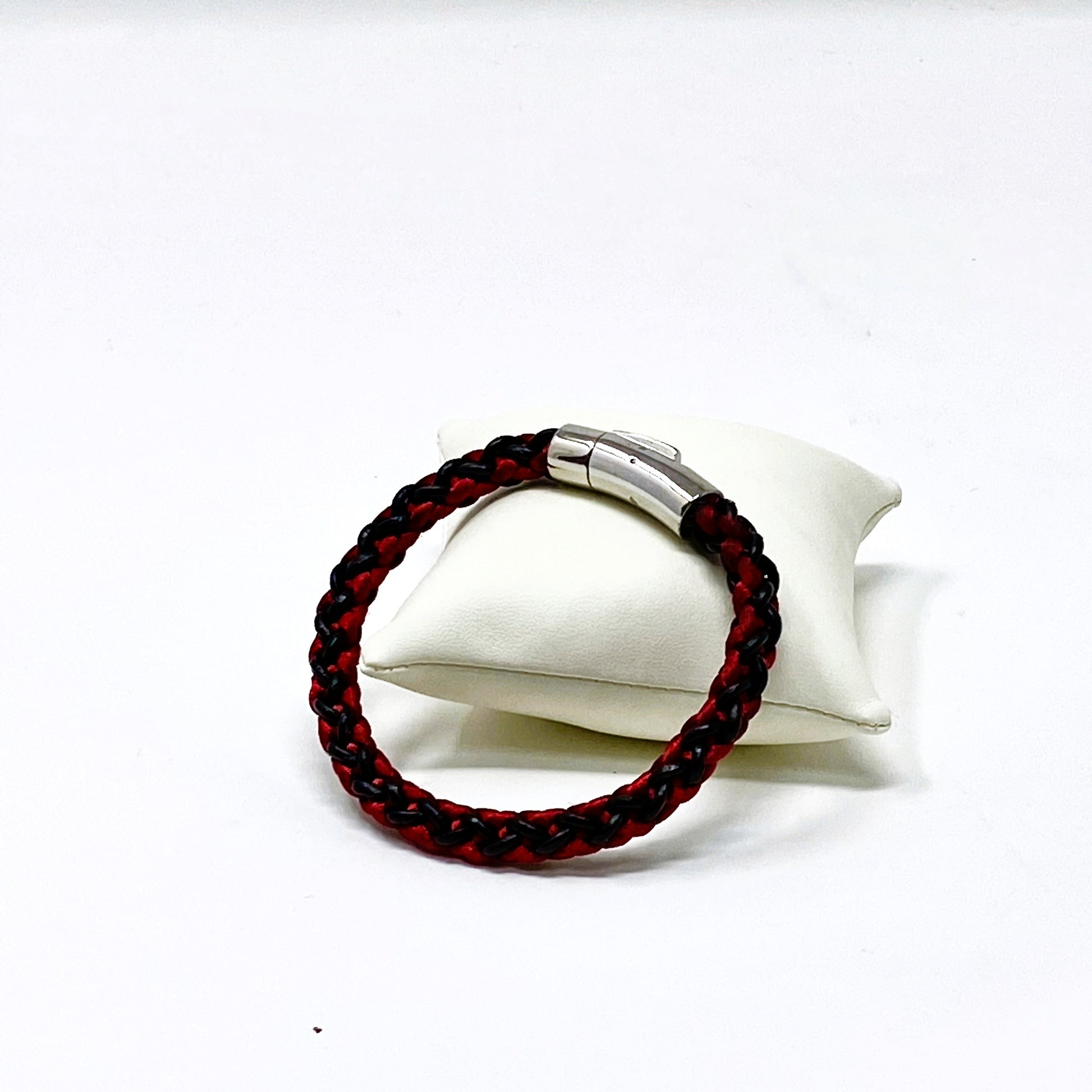 Red and black braided bracelet with silver clasp on a white stand against a white background
