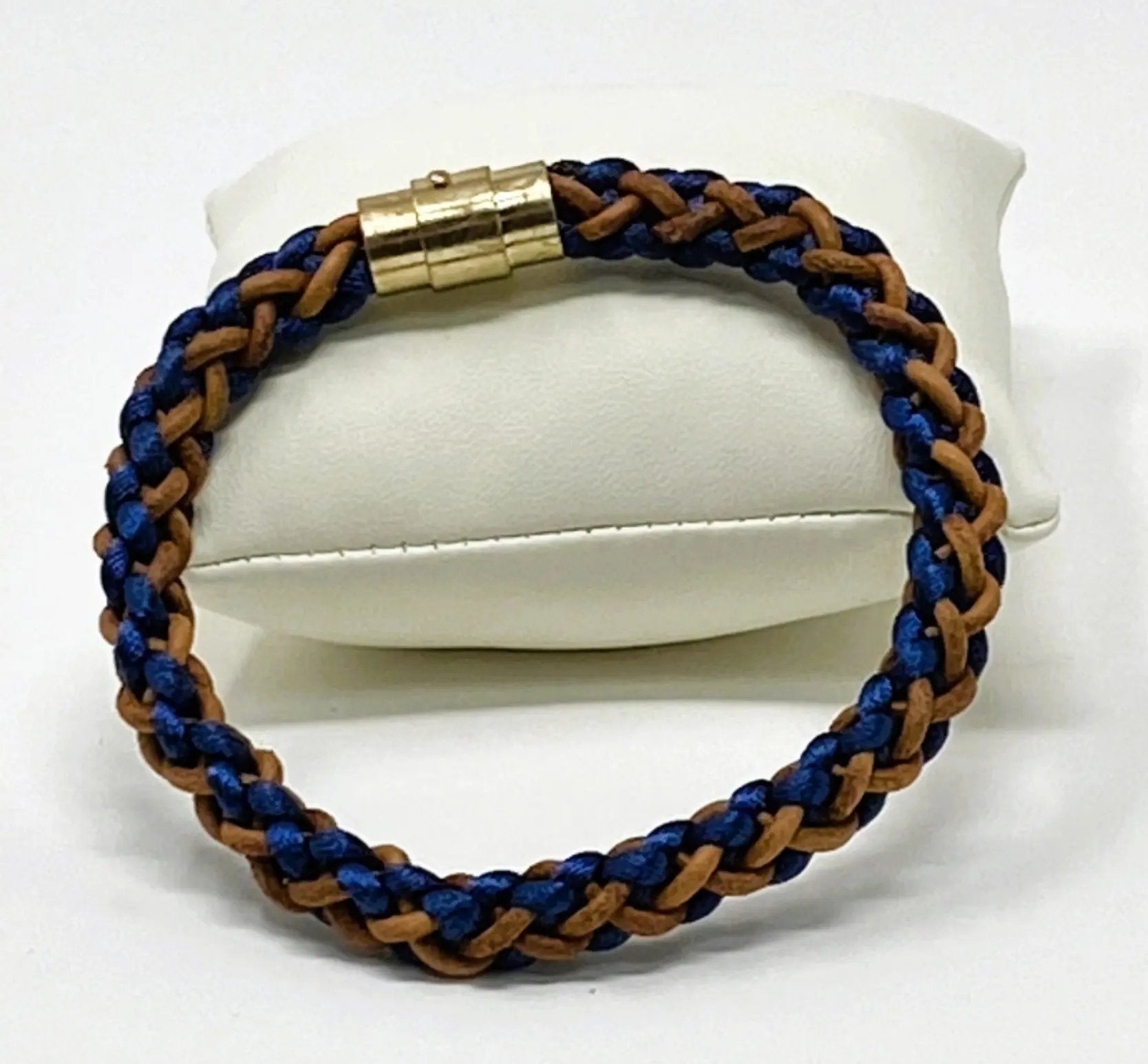 Men’s braided leather bracelet in navy blue and brown with polished gold clasp, elegantly presented on a white display cushion — handcrafted accessory for casual and smart styling.