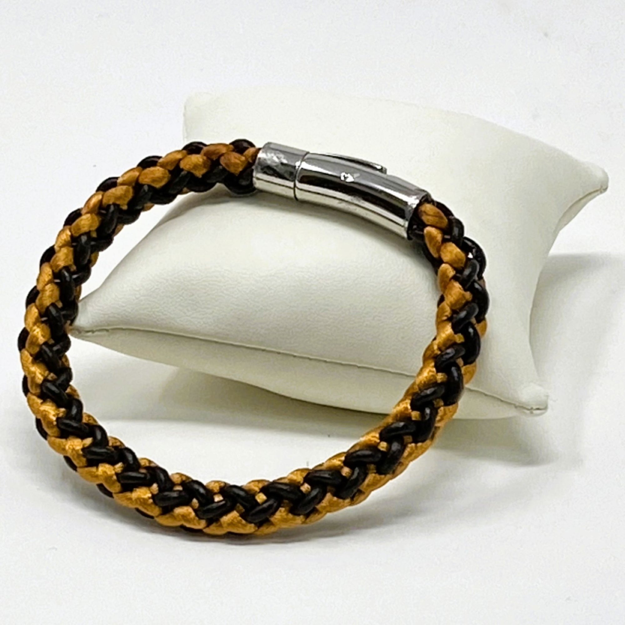 Orange and brown braided leather bracelet for men, shown on a white display cushion with polished stainless steel clasp — rugged yet refined accessory for casual wear.