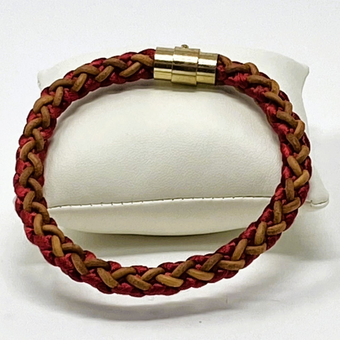 Men’s braided leather bracelet in red and brown with polished gold clasp, elegantly presented on a white display cushion — handcrafted accessory for casual and smart styling.