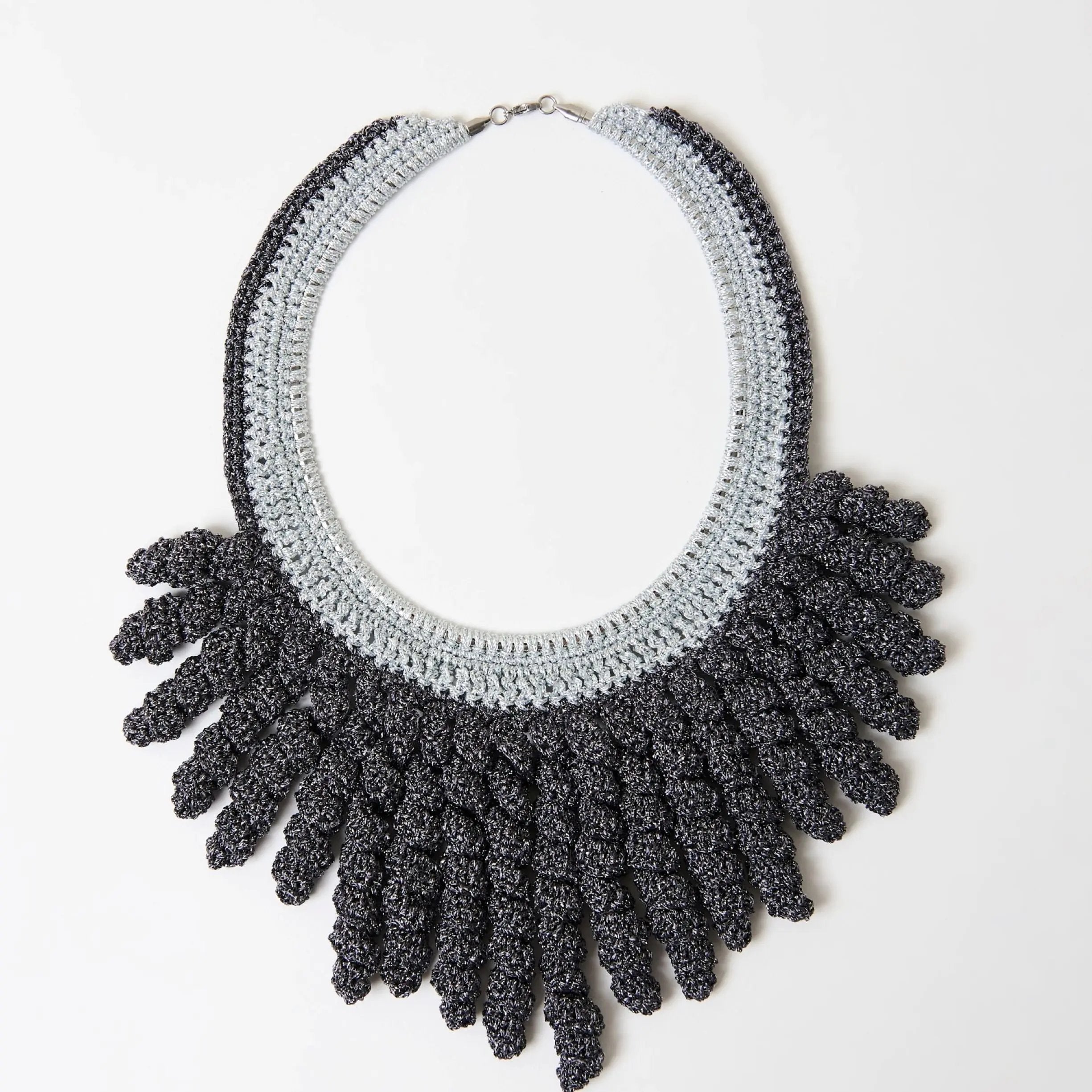 Frilled statement necklace handmade in silver and charcoal grey yarns, with bold spiral fringe fanned out on a white background.