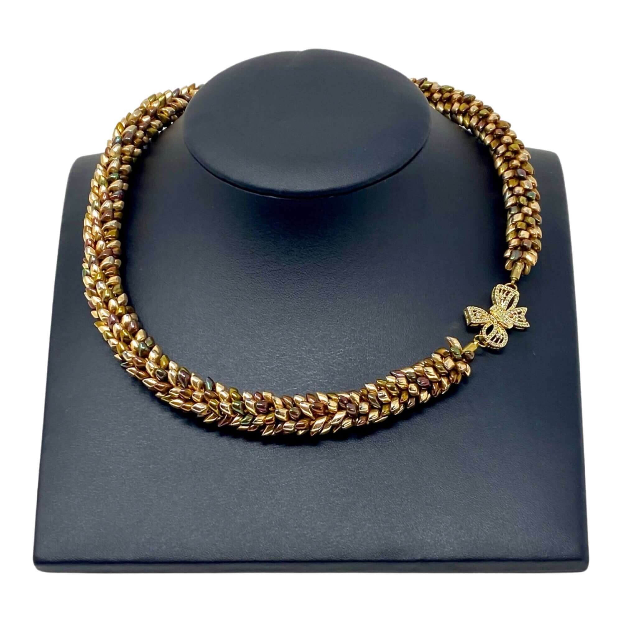 An elegant gold-toned woven necklace featuring a detailed bow-shaped charm, beautifully presented on a black jewellery bust for a classic and refined look.