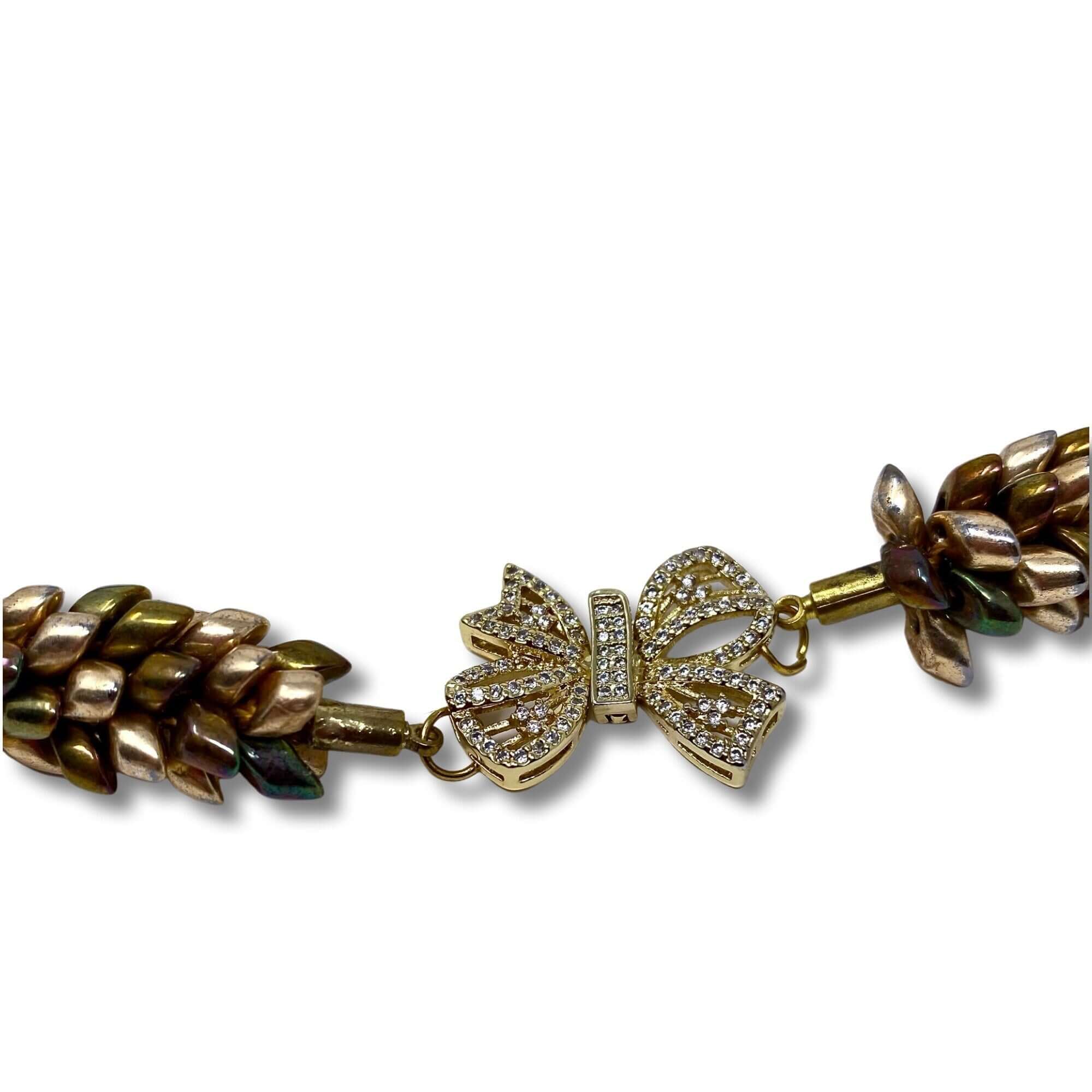 A close-up of a luxurious gold-toned woven necklace showcasing a sparkling bow-shaped charm adorned with intricate crystal detailing, emphasizing its elegant craftsmanship against white background.