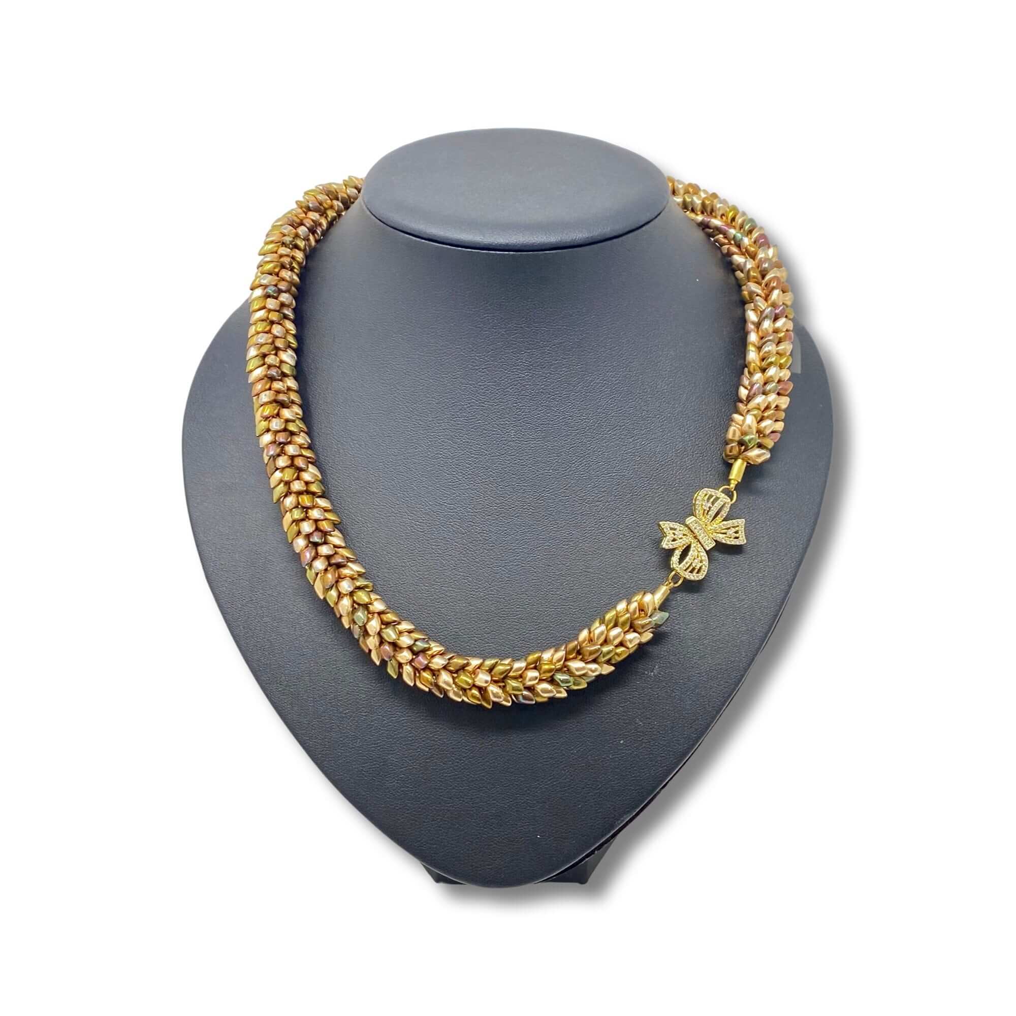 An elegant gold-toned woven necklace featuring a detailed bow-shaped charm, beautifully presented on a black jewellery bust for a classic and refined look.