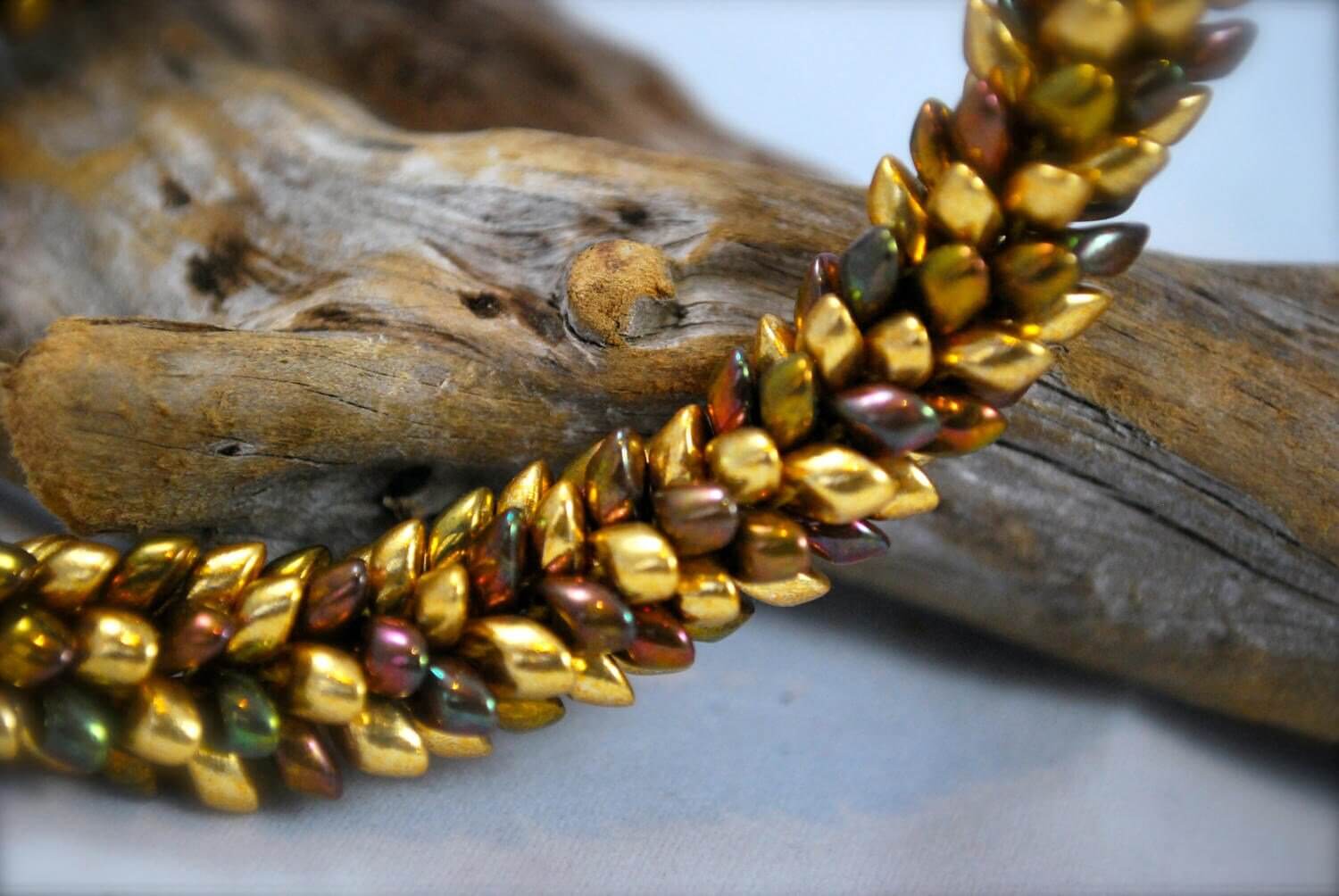 A close-up of a luxurious gold-toned woven necklace against a driftwood.