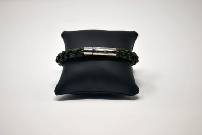 A braided bracelet with green and brown tones, featuring a stainless steel magnetic clasp, elegantly displayed on a black leather cushion against a white background.