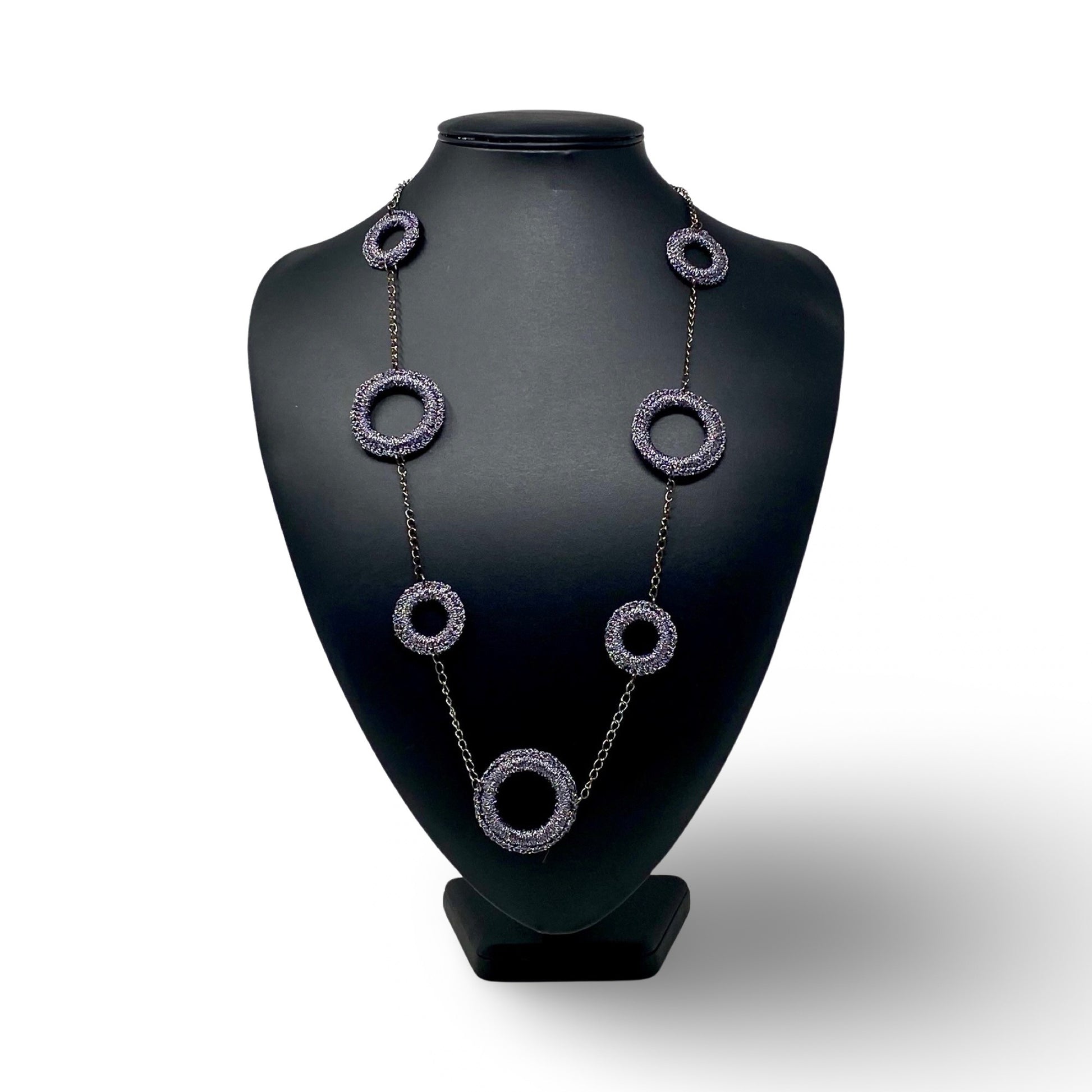 A statement necklace displayed on a black mannequin bust, featuring textured dark metallic circular links connected by a delicate chain. The design emphasizes modern elegance and bold, geometric elements, ideal for contemporary fashion styles.