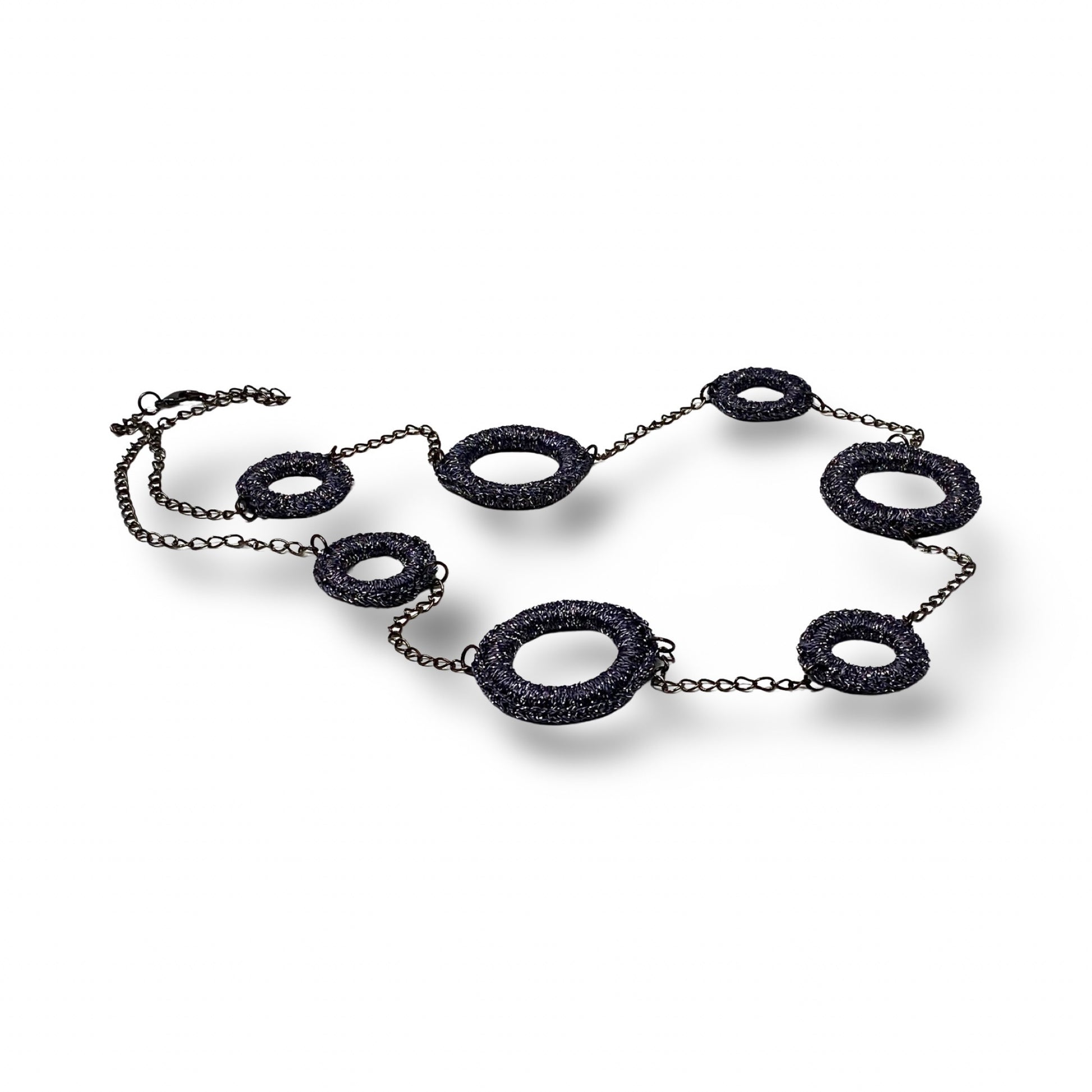 A statement necklace featuring textured dark metallic circular links of varying sizes, connected by a delicate chain. The unique design showcases an industrial-chic aesthetic, perfect for bold and contemporary fashion styles.