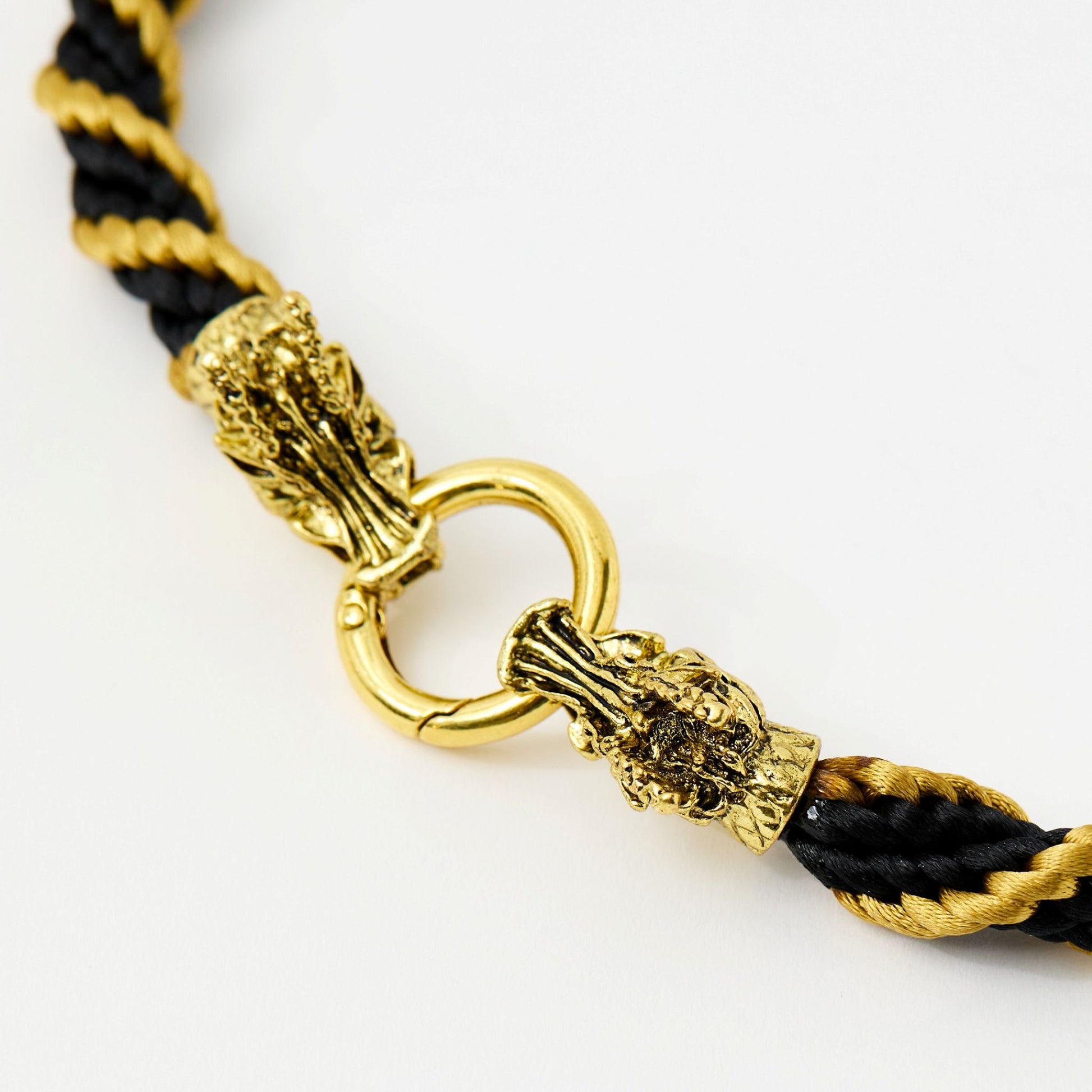 Side close-up of detailed gold-tone dragon head clasp securing a black and gold satin rope necklace.