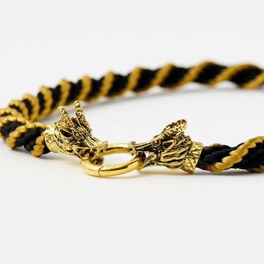 Angled view of dragon head clasp with intricate scale and horn details, joined by a round gold ring on a black and gold twist necklace.
