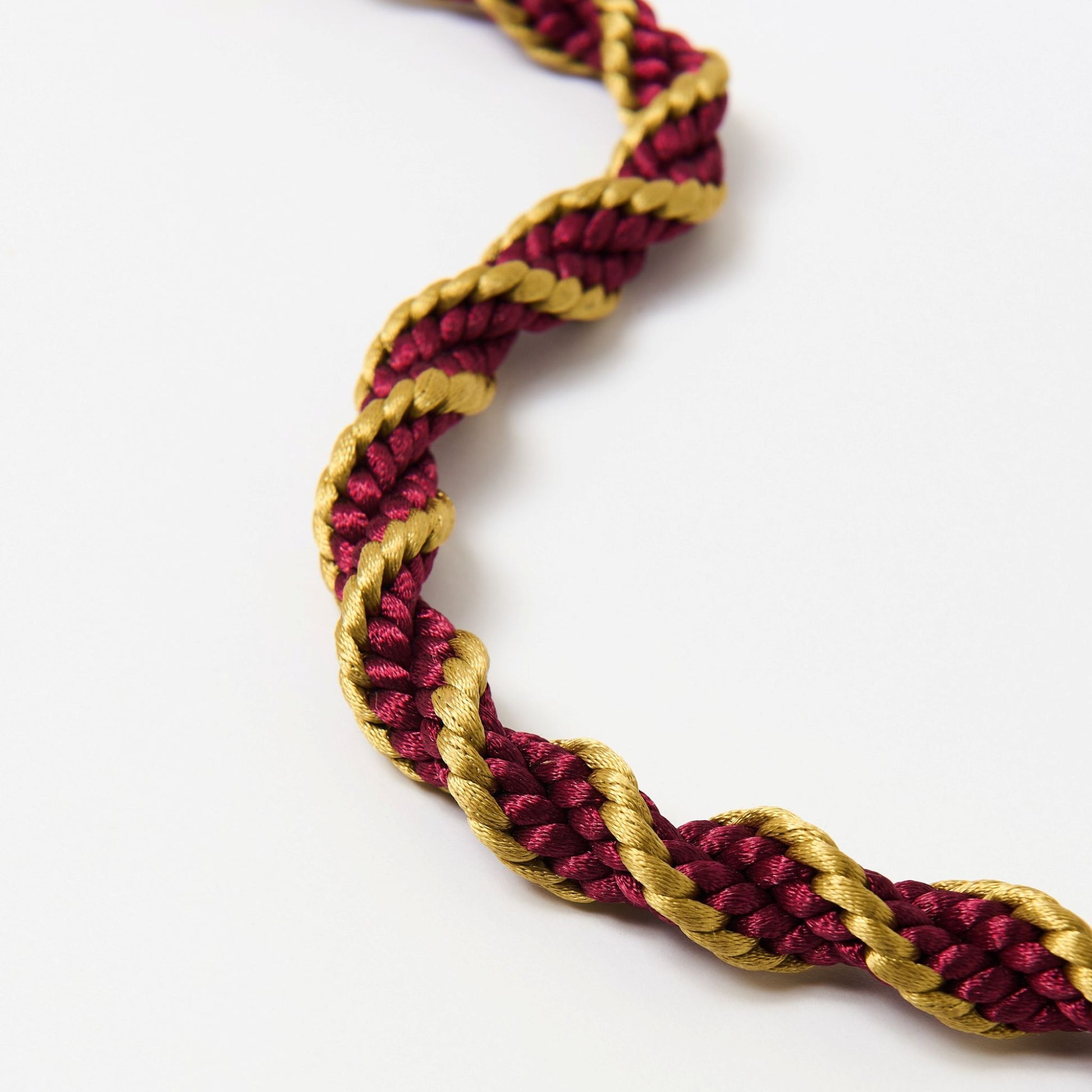 Macro detail of red and gold satin twist cord showing lustrous texture and tight braid.